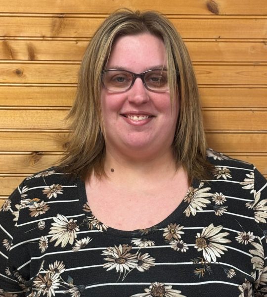 Town of Hartsville Town Clerk Ashley Gibson wearing a black shirt with white daisies in front of a wood wall