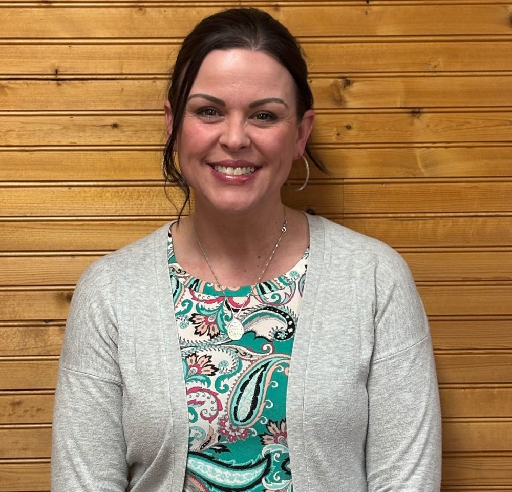 Town of Hartsville Board Member Brinette Steffey wearing a teal, white, black and pink paisley shirt with a grey sweater standing in front of a wood wall