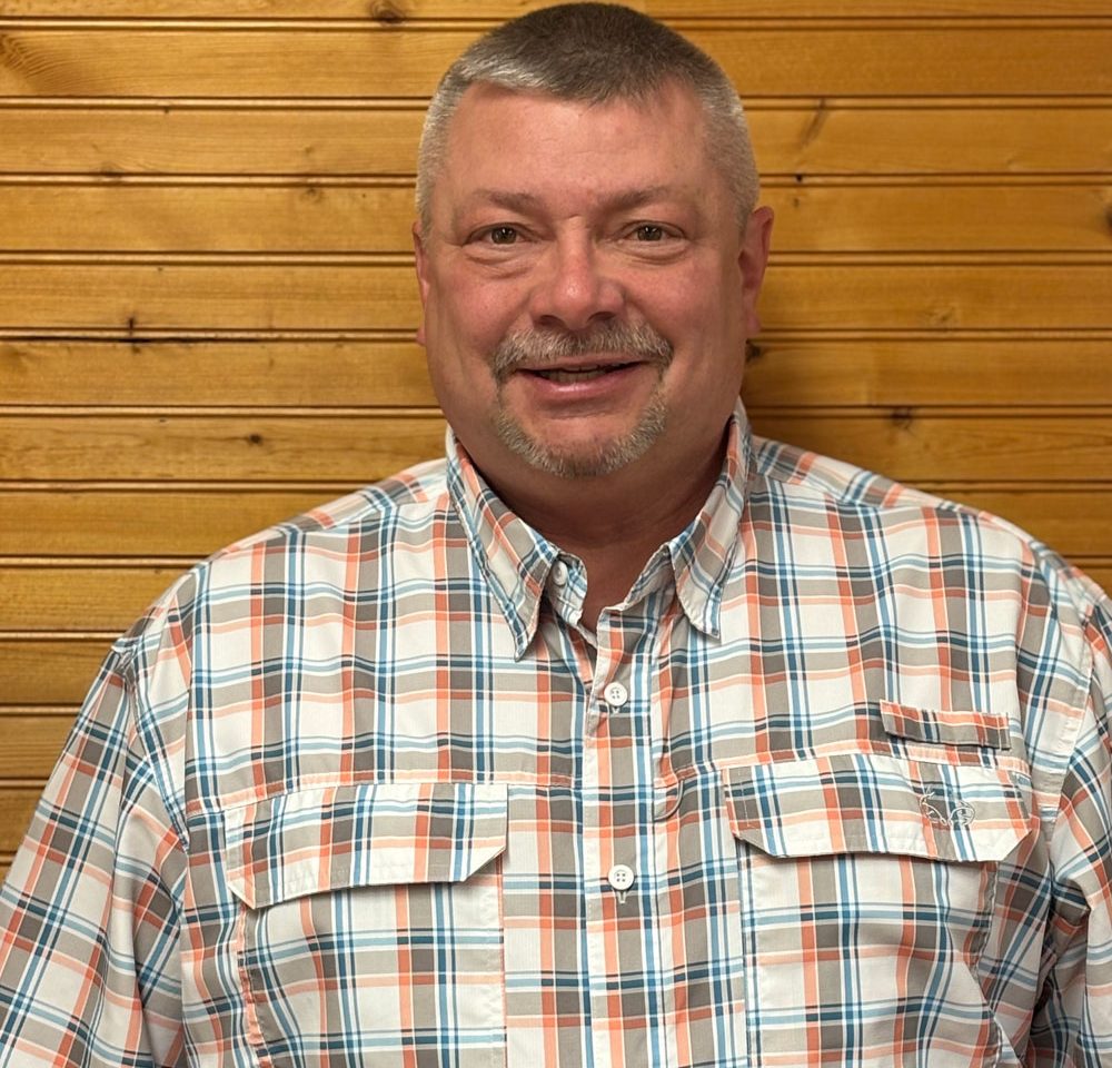 Town of Hartsville Town Supervisor David Gerhard wearing a white, grey, orange and blue checkered flannel standing in front of a wood wall.