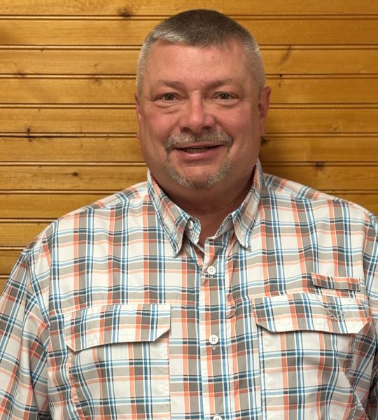 Town of Hartsville Town Supervisor David Gerhard wearing a white, grey, orange and blue checkered flannel standing in front of a wood wall.