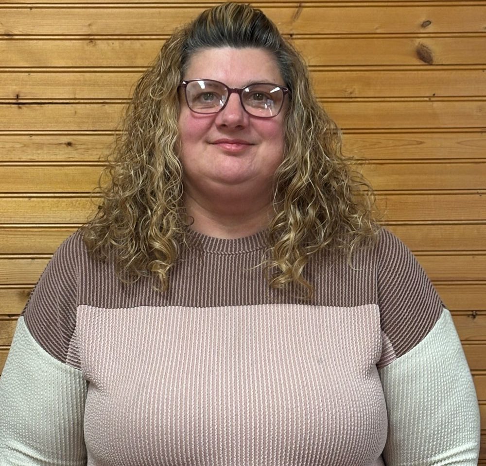 Town of Hartsville Board Member Heidi Margeson wearing a pink, white and brown sweater standing in front of a wood wall
