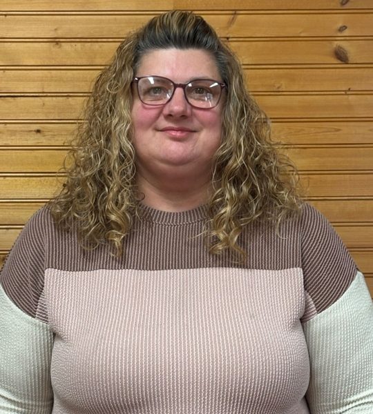 Town of Hartsville Board Member Heidi Margeson wearing a pink, white and brown sweater standing in front of a wood wall