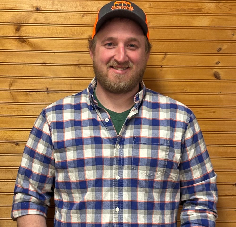 Town of Hartsville Highway Superintendent Jeffrey Getman wearing a blue, white, grey and orange flannel, a ballcap and standing in front of a wood wall