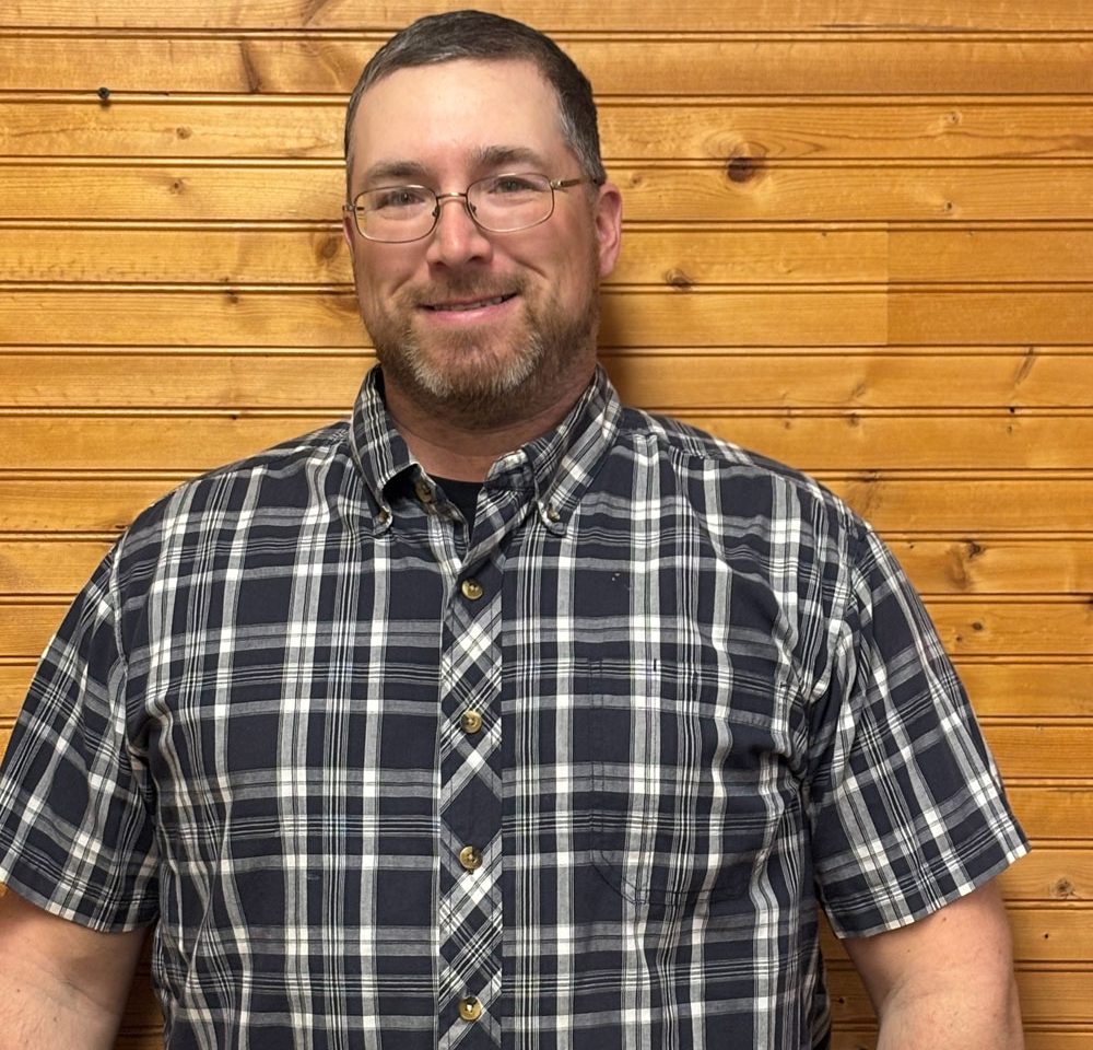 Town of Hartsville Code Enforcer Sam Koehler wearing a blue and white flannel and standing in front of a wood wall