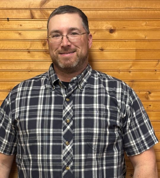 Town of Hartsville Code Enforcer Sam Koehler wearing a blue and white flannel and standing in front of a wood wall