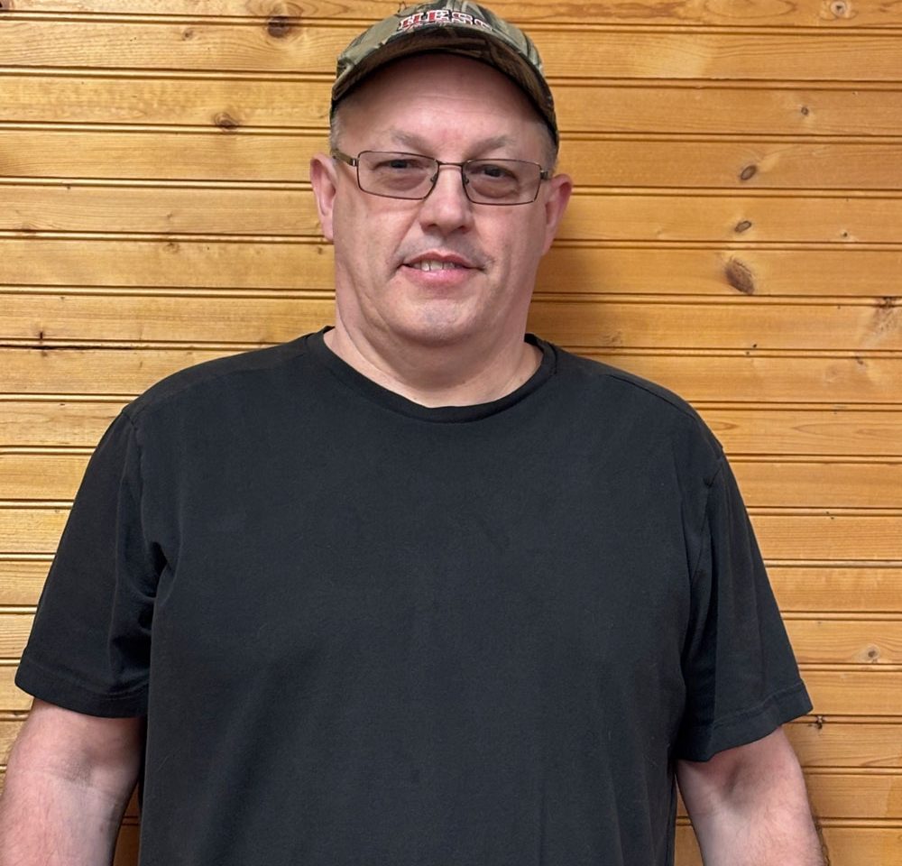 Town of Hartsville Board Member Leon Woodworth Jr. wearing a black t-shirt, a ballcap and standing in front of a wood wall
