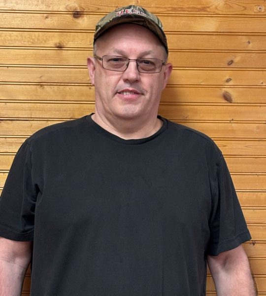 Town of Hartsville Board Member Leon Woodworth Jr. wearing a black t-shirt, a ballcap and standing in front of a wood wall